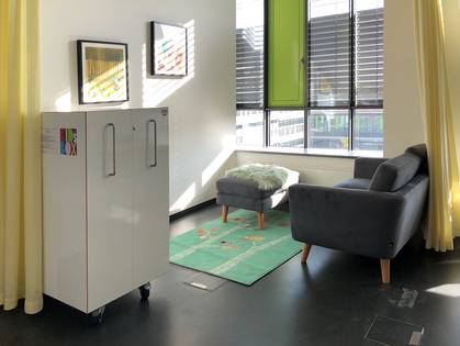 The parenting room’s resting area equipped with a couch, the KidsBox containing various equipment, carpet and dividing curtain